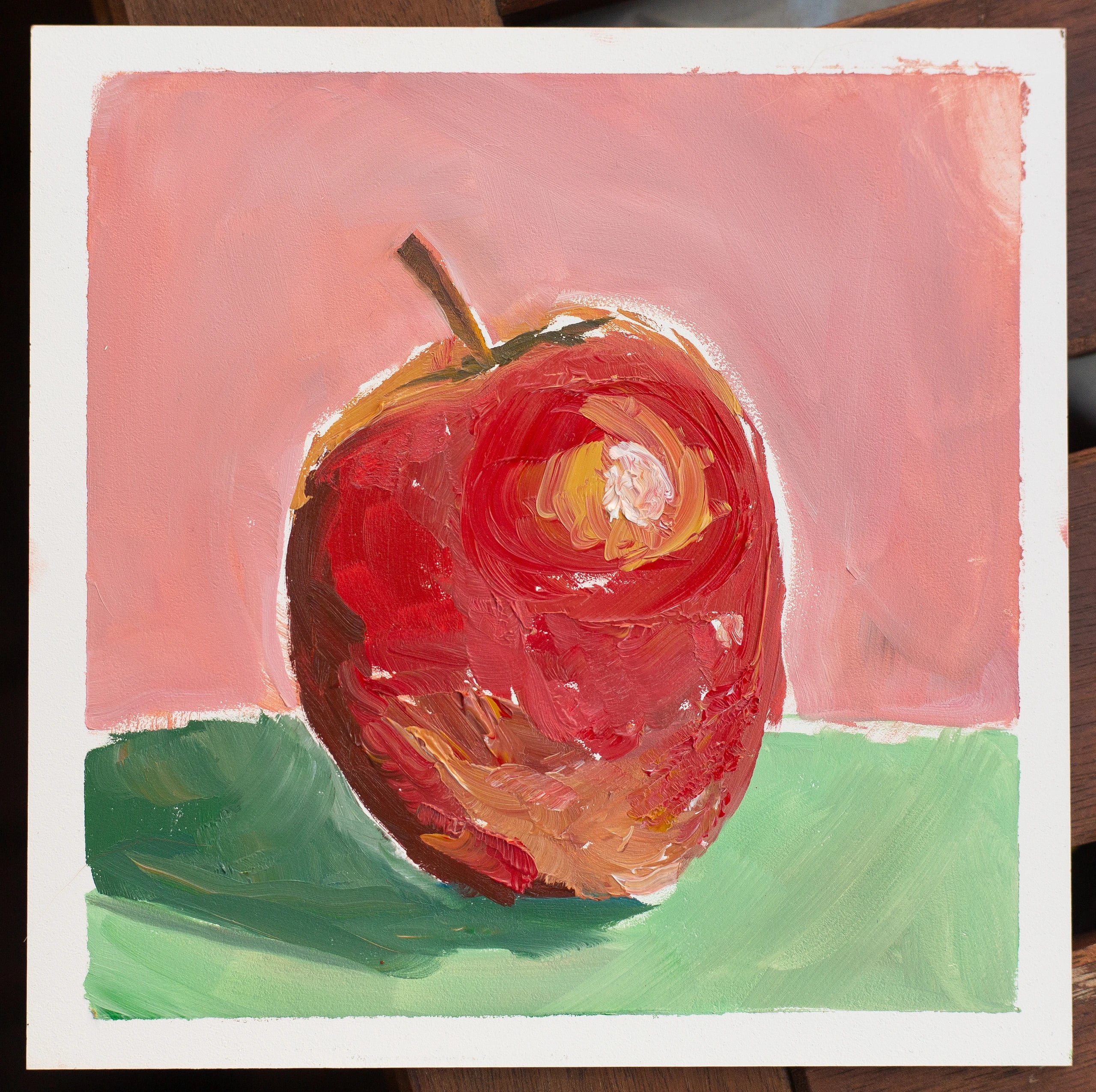 Oil painting of a glossy red apple with a bright highlight, on a green surface against a pink background.