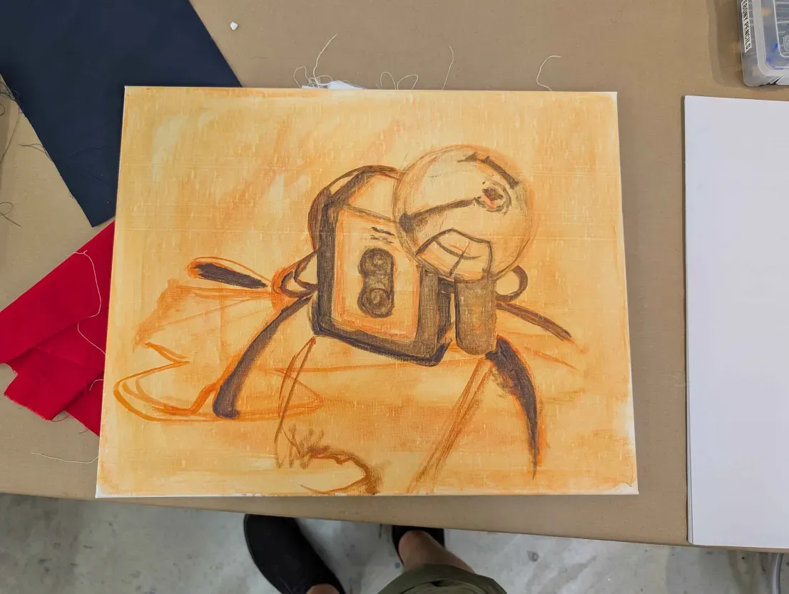 Early stage of the camera painting: a burnt sienna wash and line sketch on canvas, seen from above.