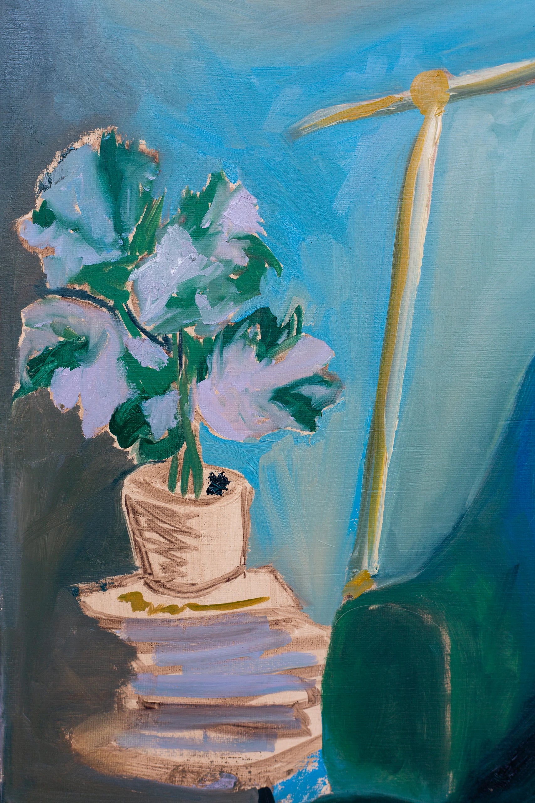 Close-up of the side table: a potted plant with pale leaves on a stack of books beside a lamp stand.